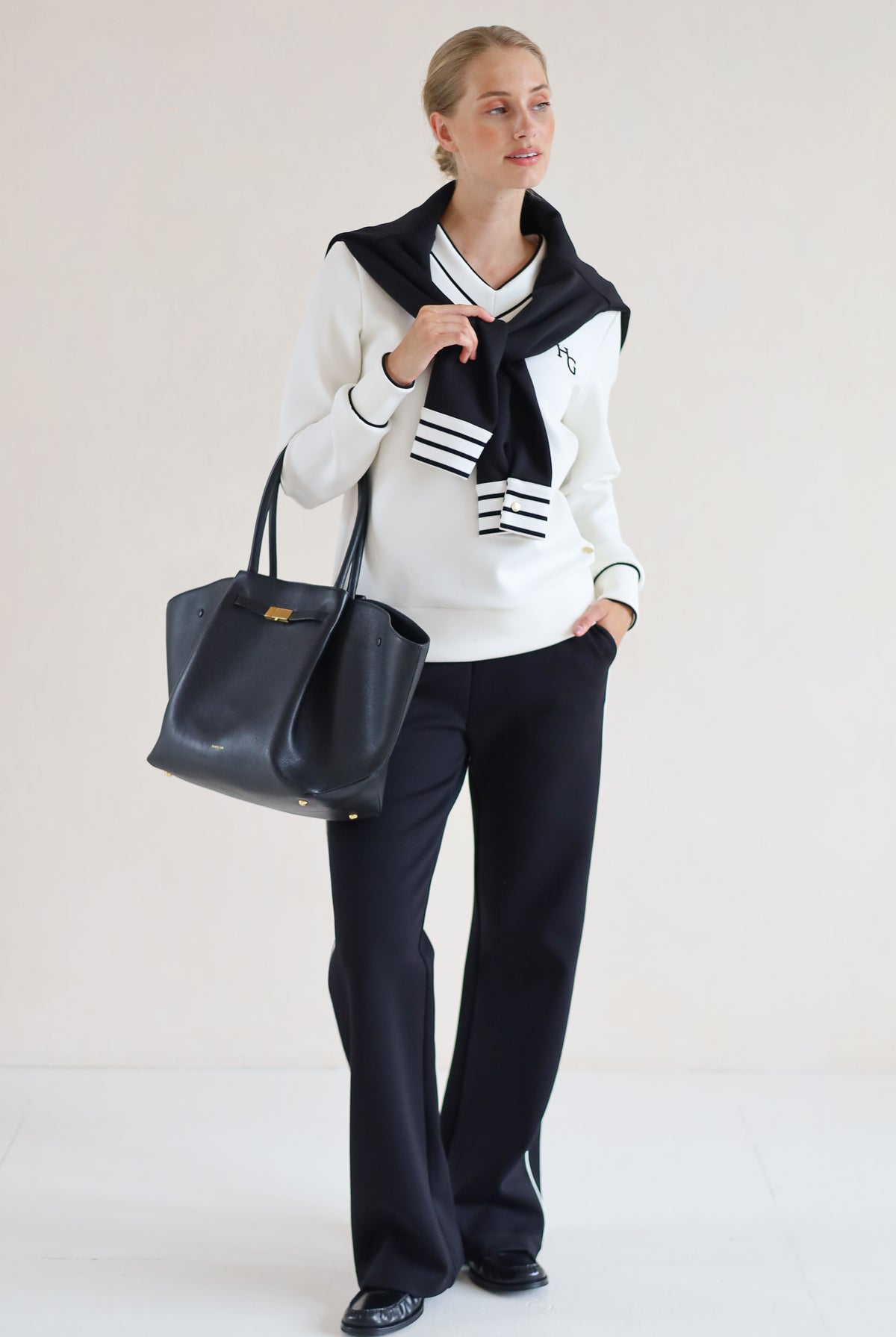 House of Gravity V-Neck Sweater in Off-White Marble and Black paired with the Wide Leg Trouser in Black, styled with a knit sweater and tote bag.