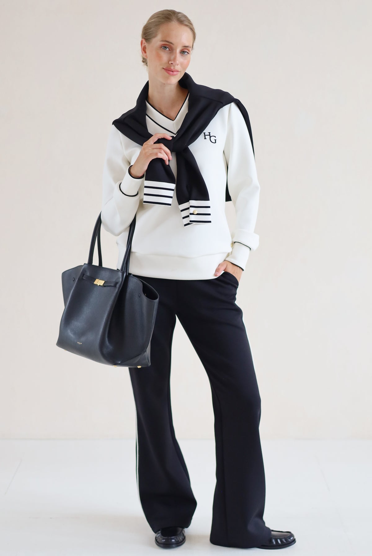 House of Gravity V-Neck Sweater in Off-White Marble and Black paired with the Wide Leg Trouser in Black, styled with a striped knit draped over the shoulders.