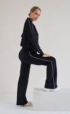 A woman models a matching black set with white piping details, posing on a white block against a plain light background.