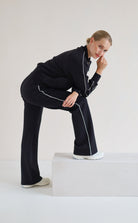 A woman modeling a black athletic set with white piping details, posing on a white platform against a light gray studio background.