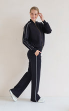 A woman modeling a matching black se with white piping details, featuring a bomber jacket and wide-leg pants, set against a plain light background.