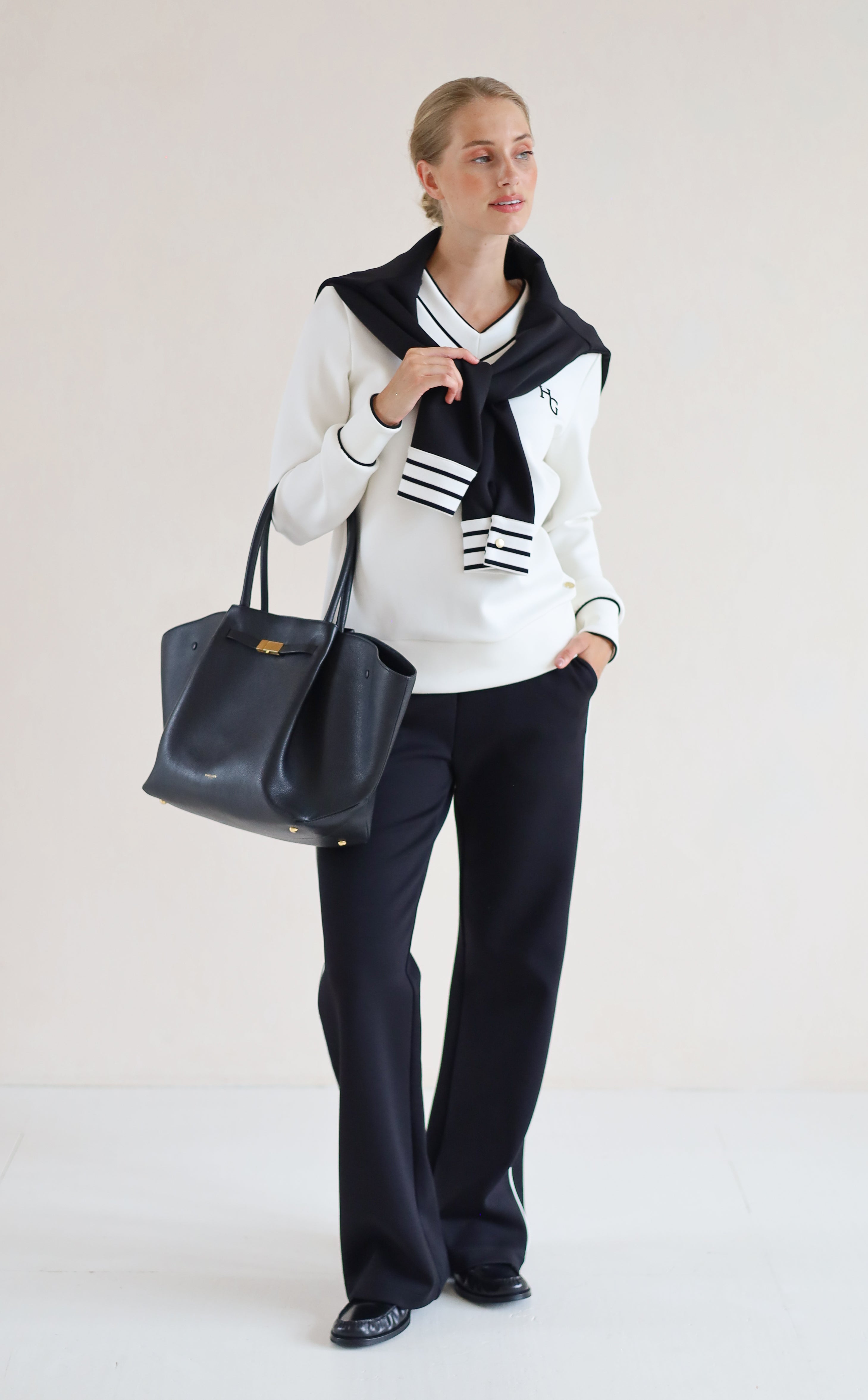 House of Gravity V-Neck Sweater in Off-White Marble and Black paired with the Wide Leg Trouser in Black, styled with a knit sweater and tote bag.