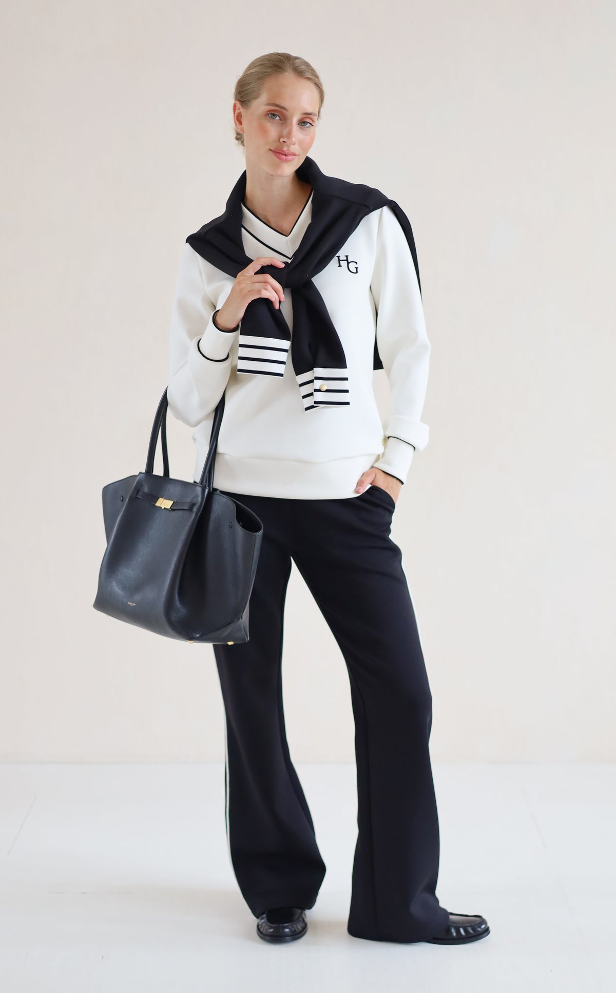 House of Gravity V-Neck Sweater in Off-White Marble and Black paired with the Wide Leg Trouser in Black, styled with a striped knit draped over the shoulders.